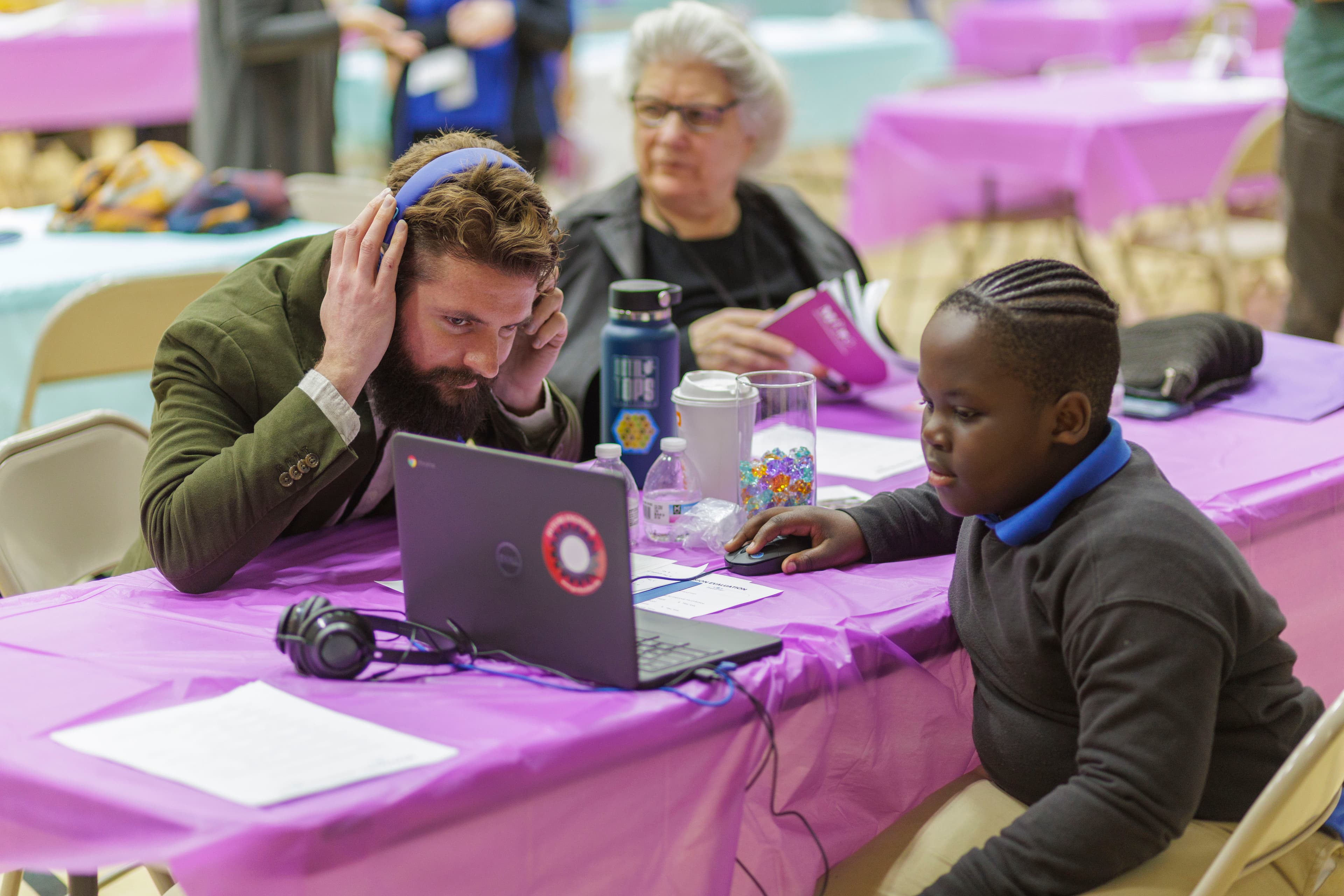 A student plays back the track they just built for a listener wearing headphones